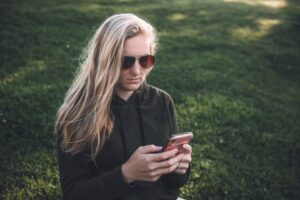 Woman in sunglasses texting on a lawn