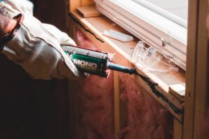 Gloved hand sealing a window with a caulking gun