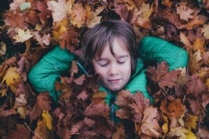 Child in a Green Jacket Lying in A Pile Of Autumn Leaves