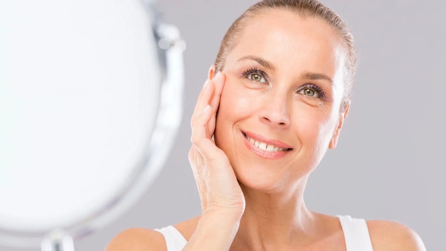 Smiling Woman Touching Her Face Near A Mirror 